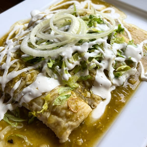 Two green enchiladas topped with sour cream, shredded lettuce, and sliced onions on a white plate.