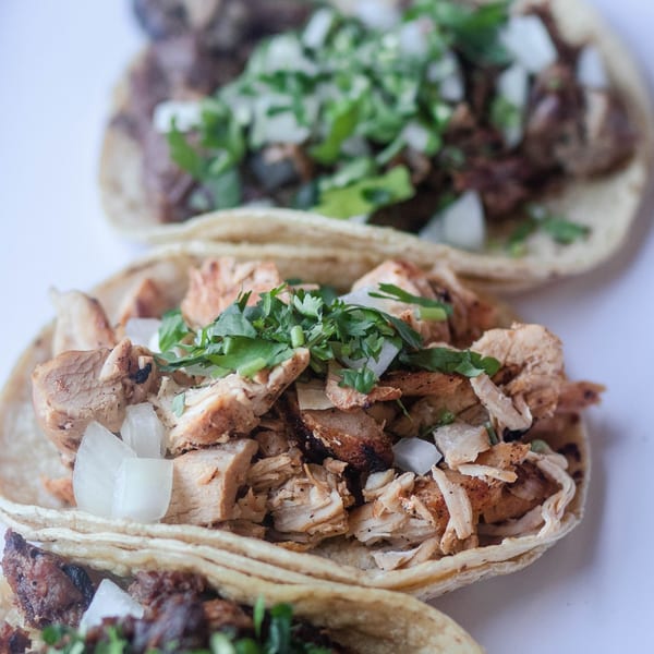 Three Mexican street tacos with various meats, onions, and cilantro on white corn tortillas.