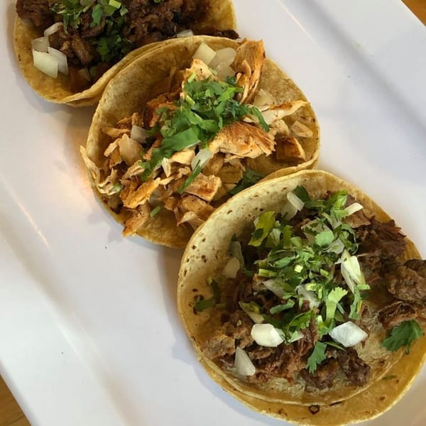 Three delicious tacos, two with beef and one with chicken, topped with cilantro and onions.