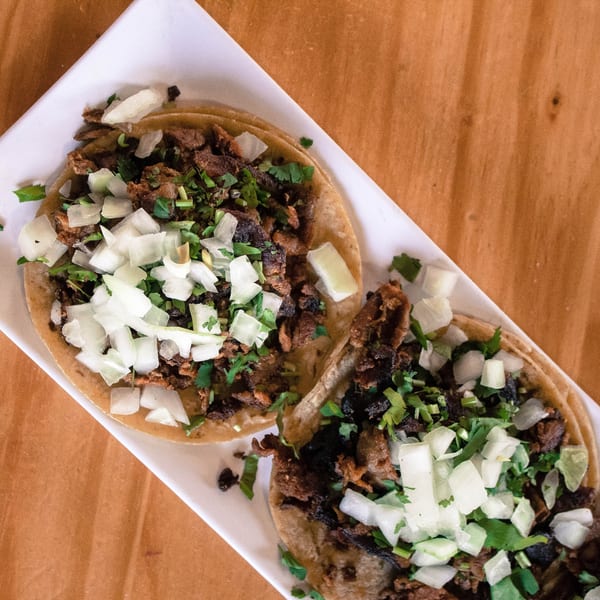 Two Mexican street tacos with chopped meat, cilantro, and diced onions on a white plate.