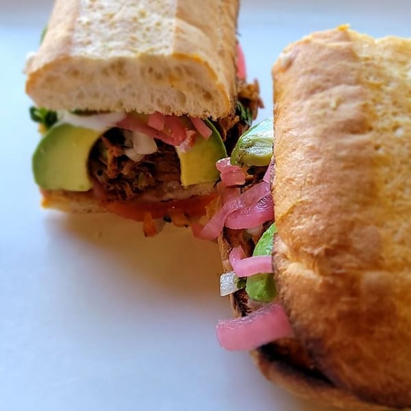 Two Mexican torta sandwiches filled with meat, avocado, onions, and pink pickled onions.