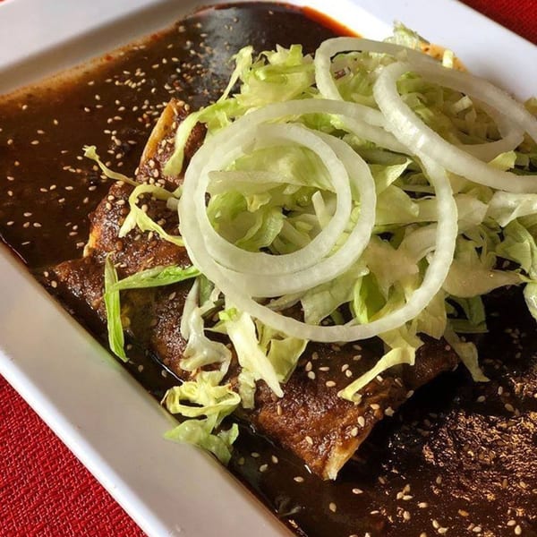 Mexican enchiladas covered in dark mole sauce, topped with shredded lettuce and white onion rings.